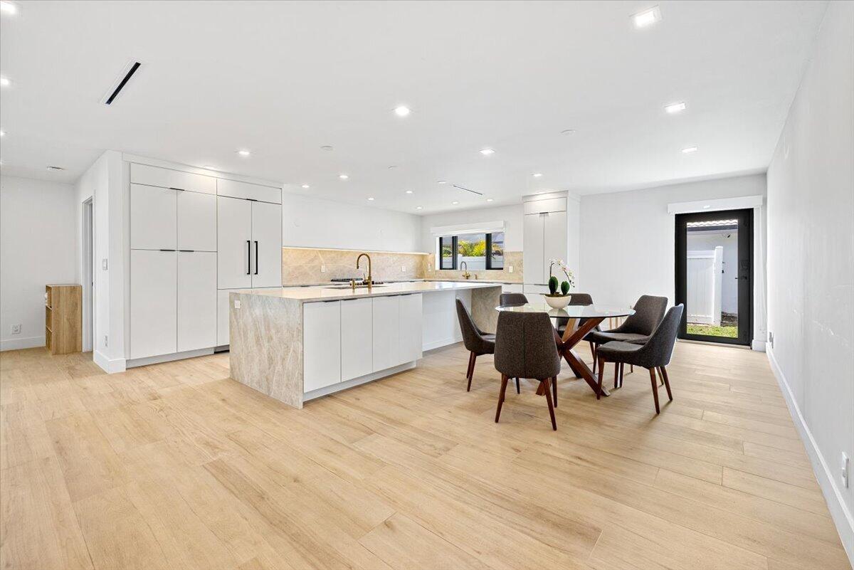A modern kitchen features white cabinetry, a marble-topped island, and a dining area with chairs — 6897 Terra Tranquila Drive, Boca Raton FL 33433, BOCA RATON, FL