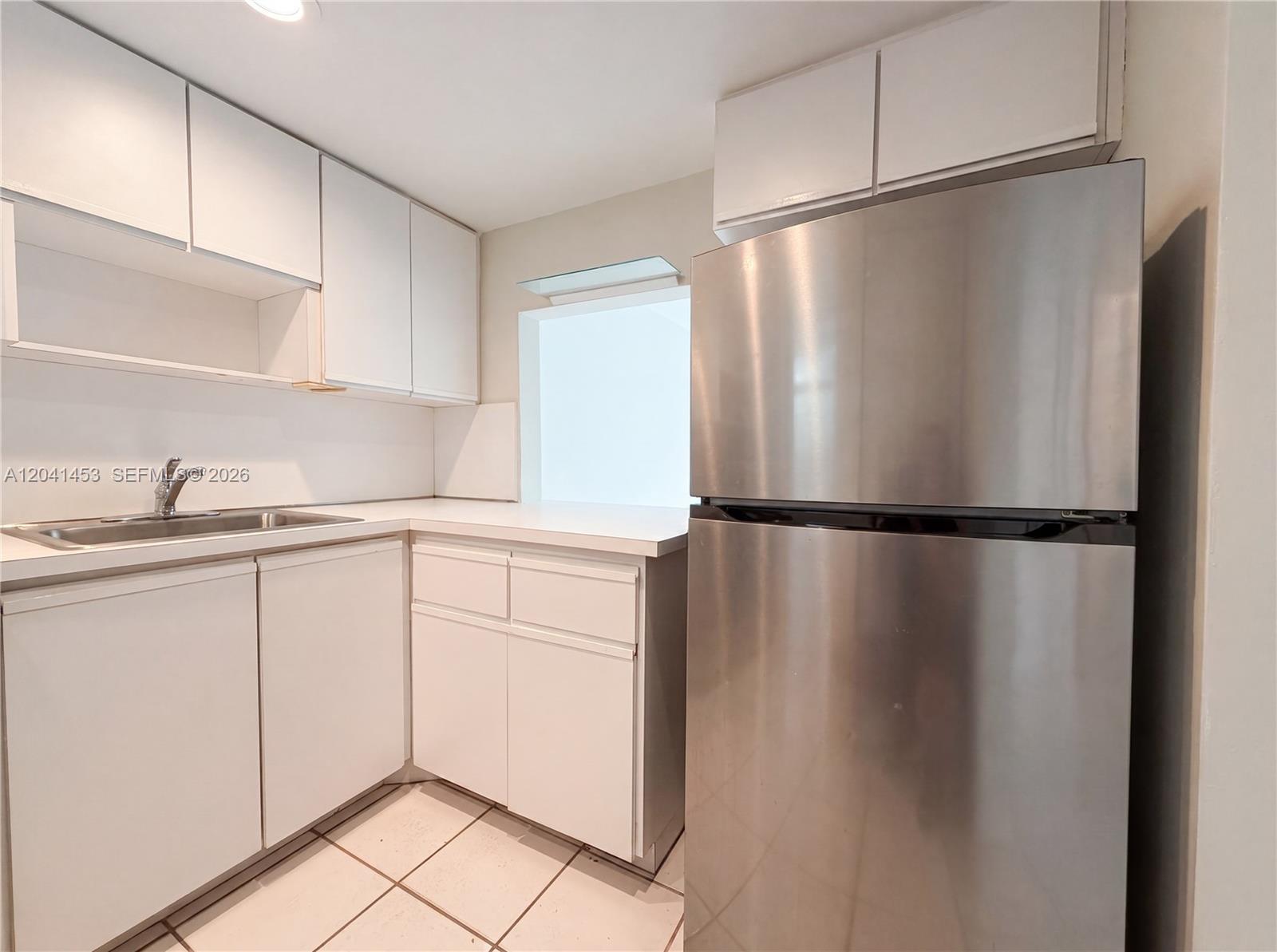 A kitchen features white cabinets, a stainless steel refrigerator, and a sink with white countertops — 200 Galen Dr # 202, Key Biscayne FL 33149, KEY BISCAYNE, FL
