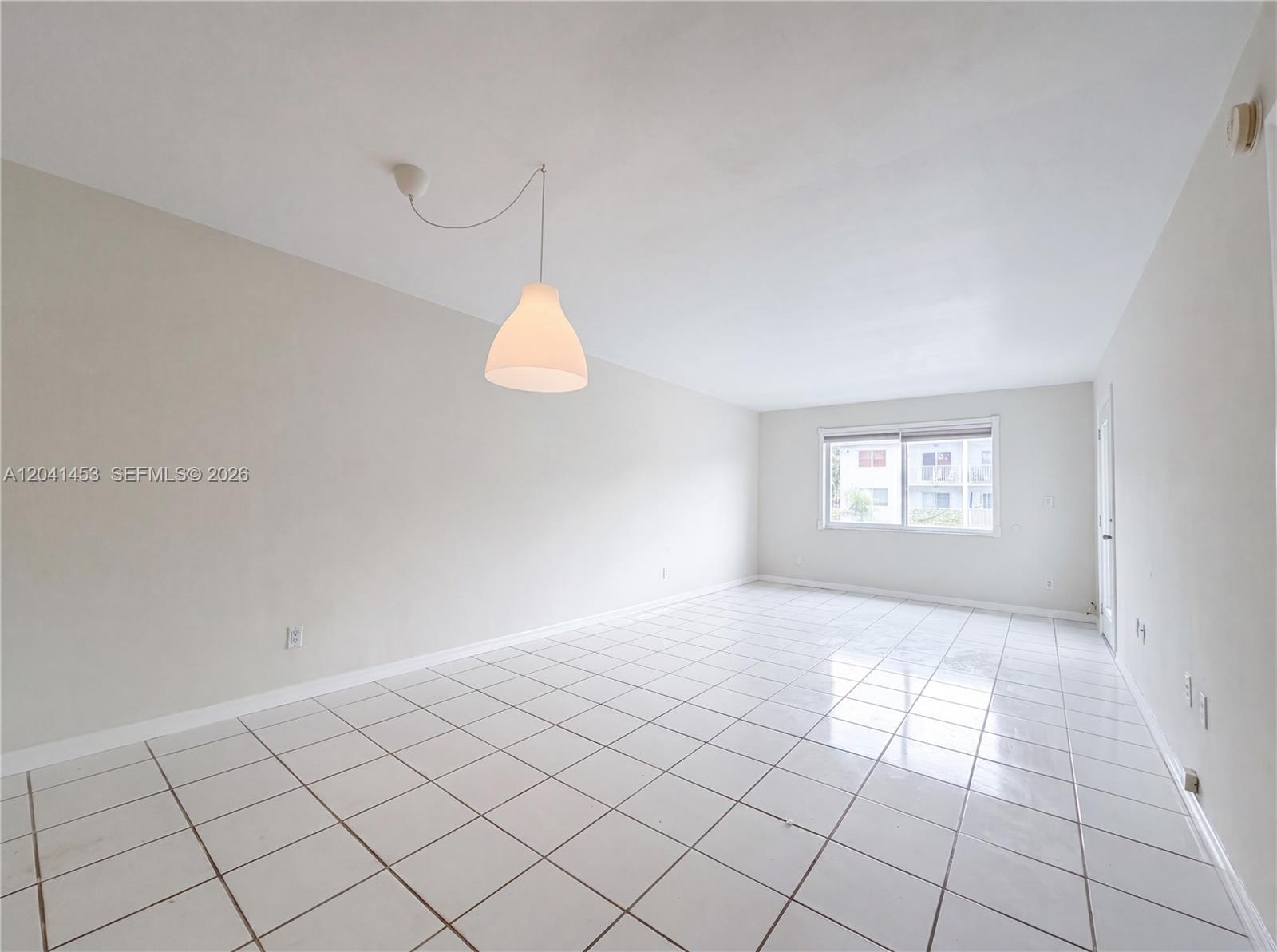 An empty room features white tiled floors, light-colored walls, and a single hanging pendant light — 200 Galen Dr # 202, Key Biscayne FL 33149, KEY BISCAYNE, FL