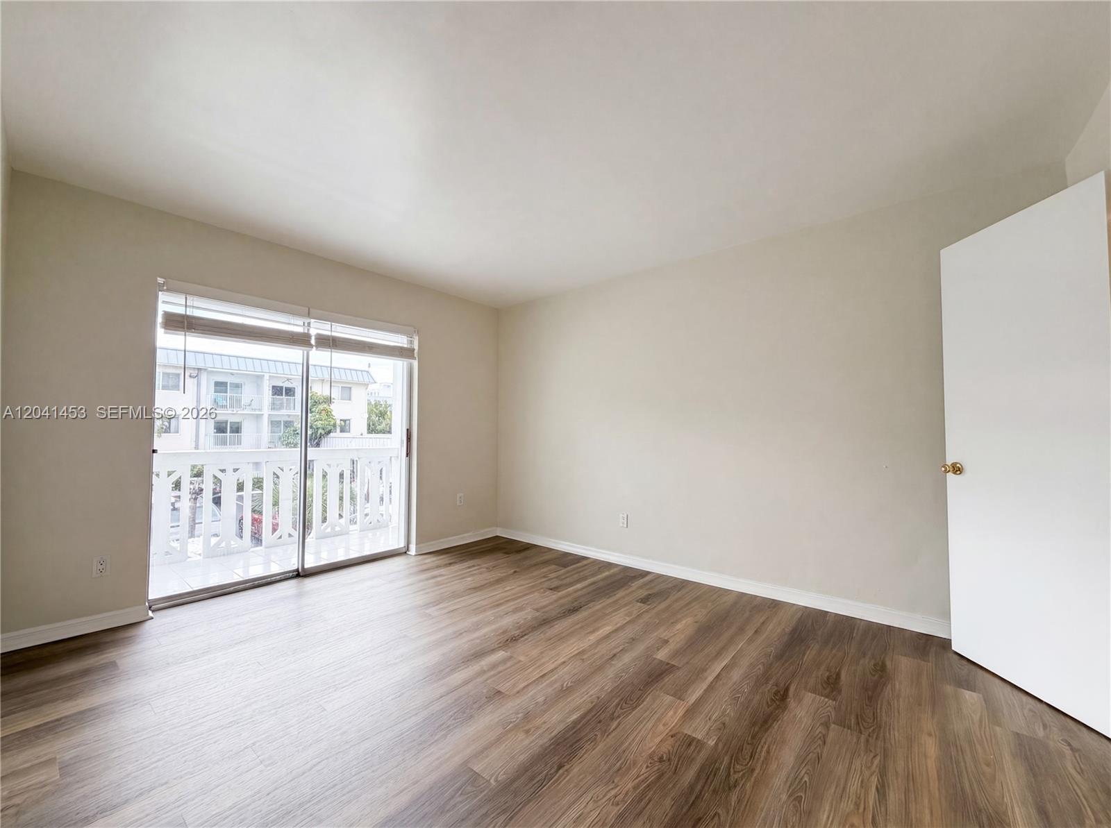 An empty bedroom features wood-look flooring, light-colored walls, and a sliding glass door to a balcony — 200 Galen Dr # 202, Key Biscayne FL 33149, KEY BISCAYNE, FL