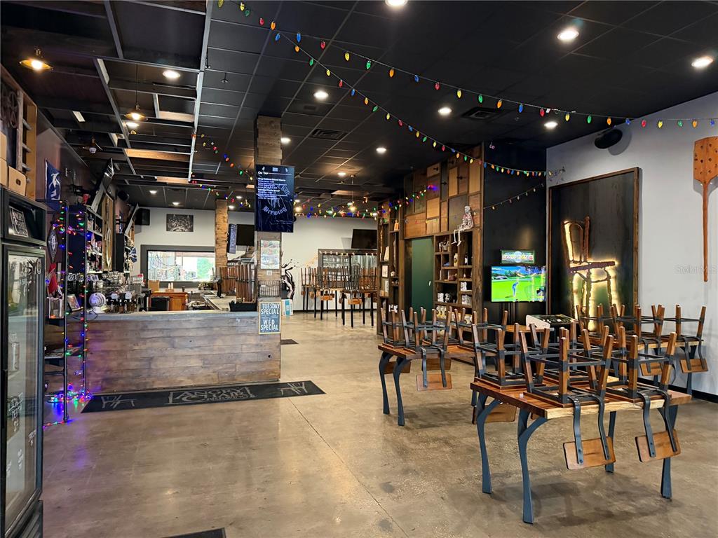 An interior view of a brewery taproom featuring a bar, tables with stacked chairs, and string lights — 4101 N FLORIDA AVENUE, TAMPA, FL