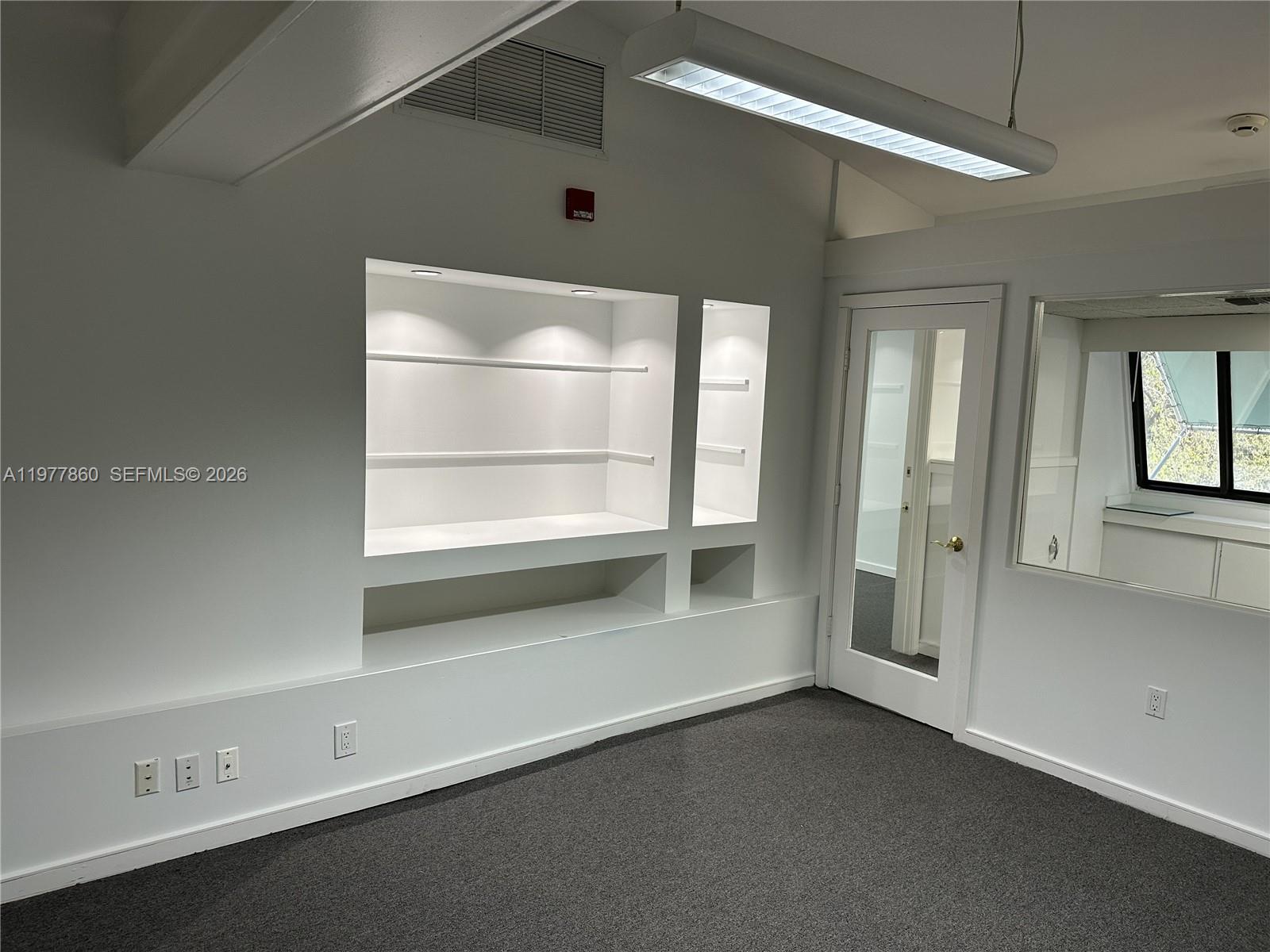 An office space features white walls, built-in shelving, a glass-paneled door, and gray carpeting — 7910 SW 57th Ave # 23, South Miami FL 33143, SOUTH MIAMI, FL