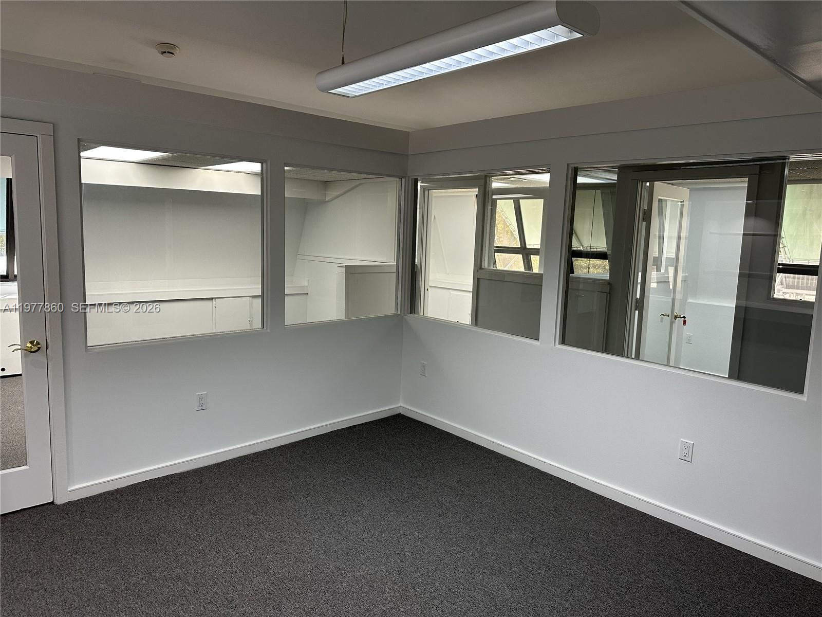 An office space features gray carpet, white walls, and large interior windows looking into adjacent rooms — 7910 SW 57th Ave # 23, South Miami FL 33143, SOUTH MIAMI, FL