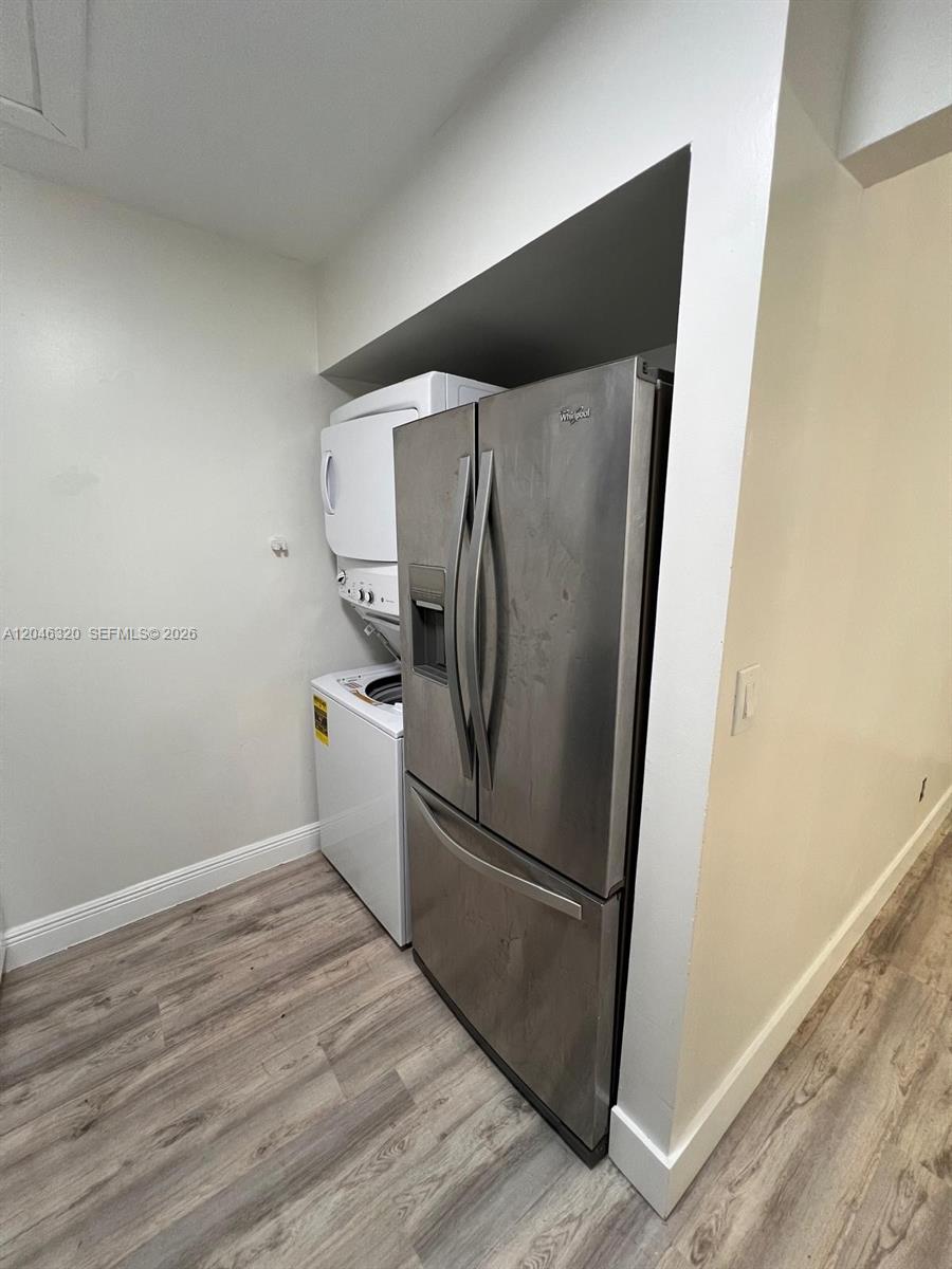 A stainless steel refrigerator stands next to a stacked washer and dryer unit — HIALEAH, FL