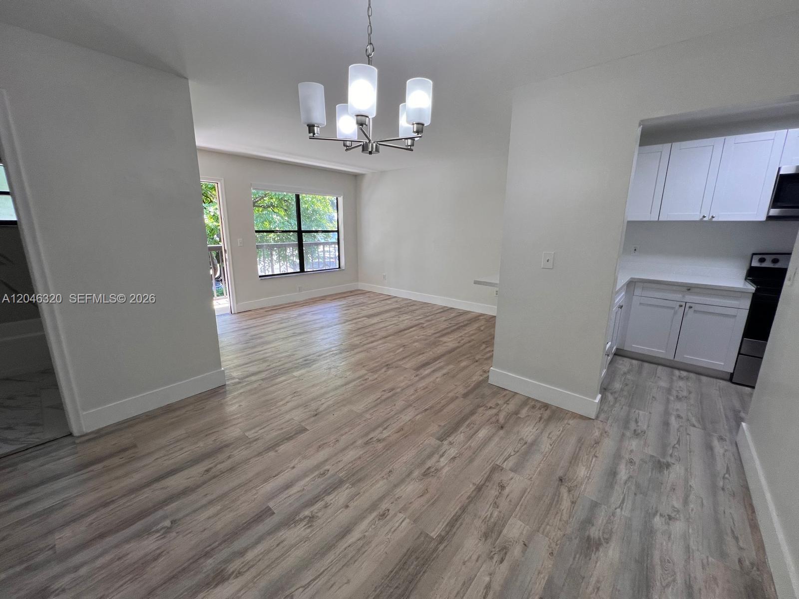 An open-concept living and dining area features light wood-look flooring and a white kitchen — HIALEAH, FL