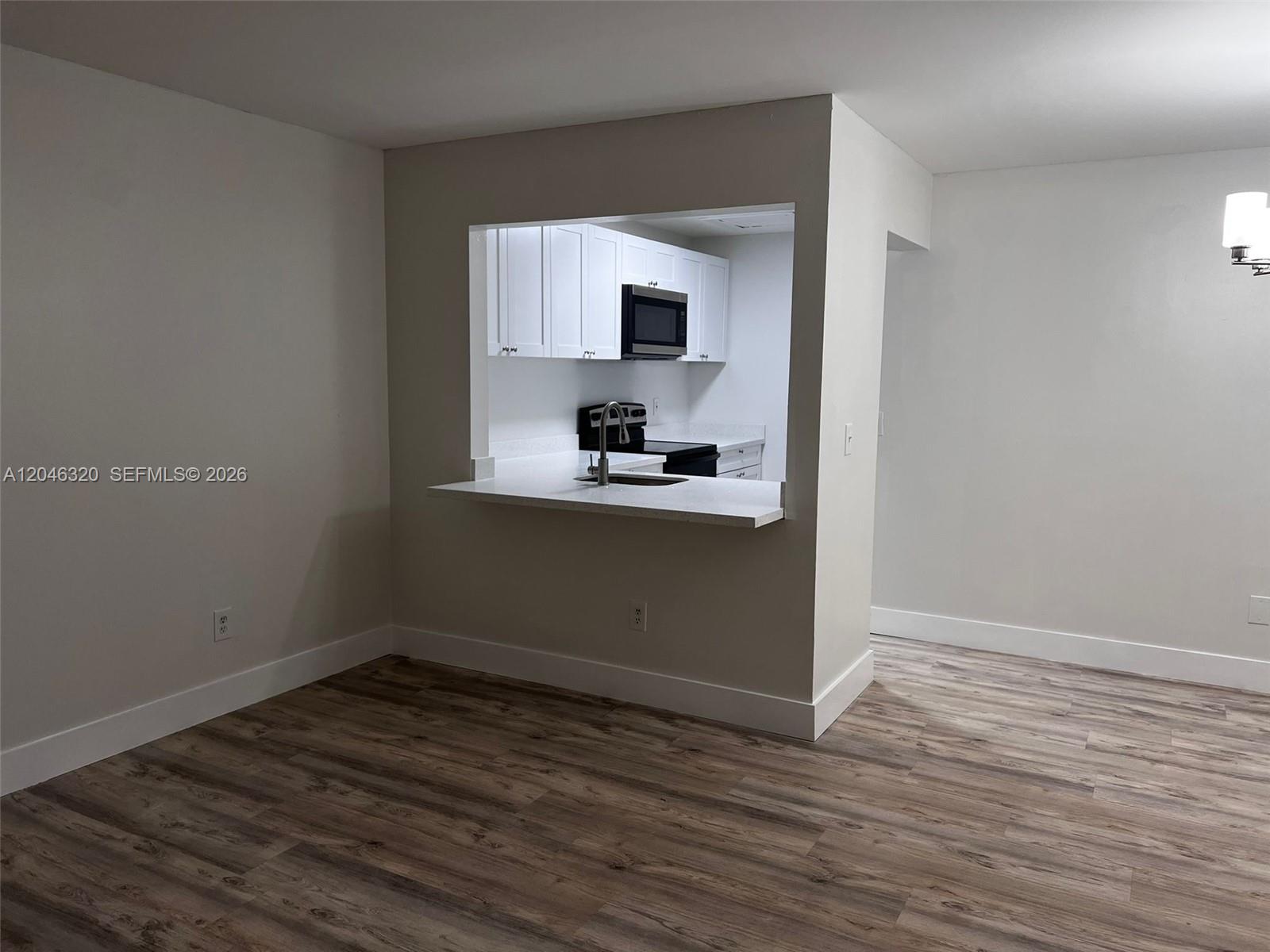 A kitchen with white cabinets and a pass-through window overlooks a room with wood-look flooring — HIALEAH, FL