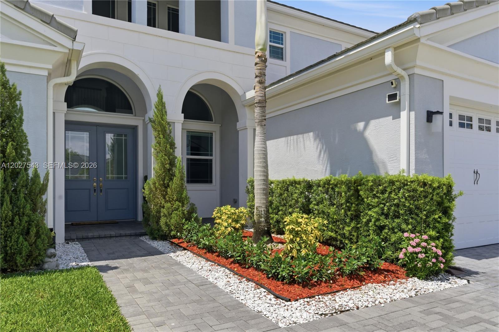 The exterior of a two-story house features a blue double door, arched entry, and landscaping — 15943 Whippoorwill CIR, Westlake FL 33470, WESTLAKE, FL