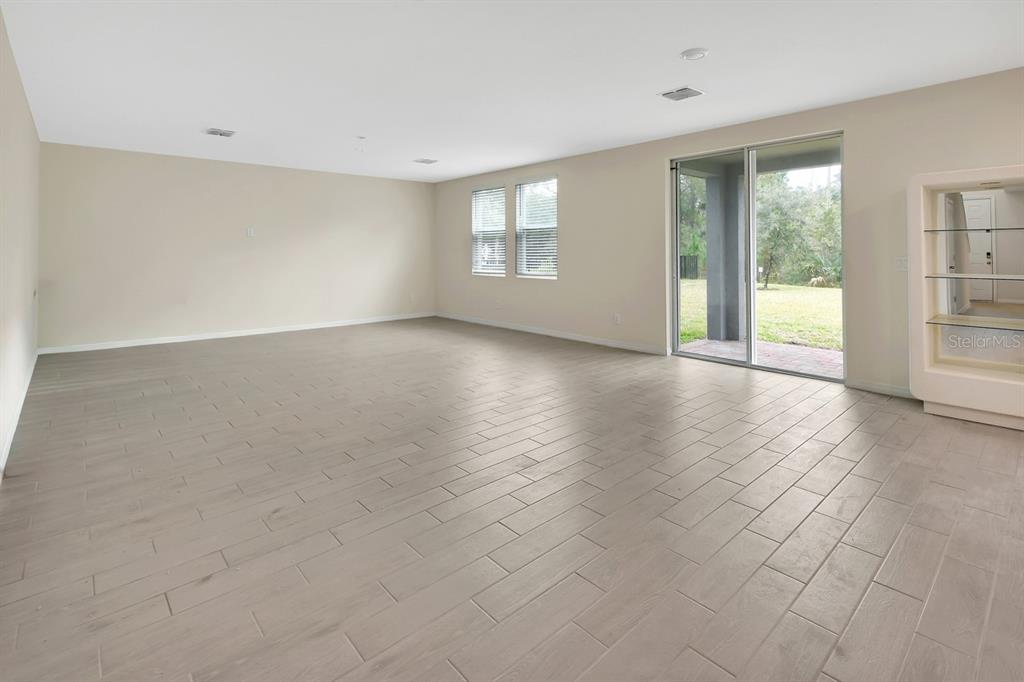 An empty living room features light-colored tile flooring, beige walls, and a sliding glass door — 335 NW SARAH NICOLE WAY, NEW SMYRNA BEACH, FL