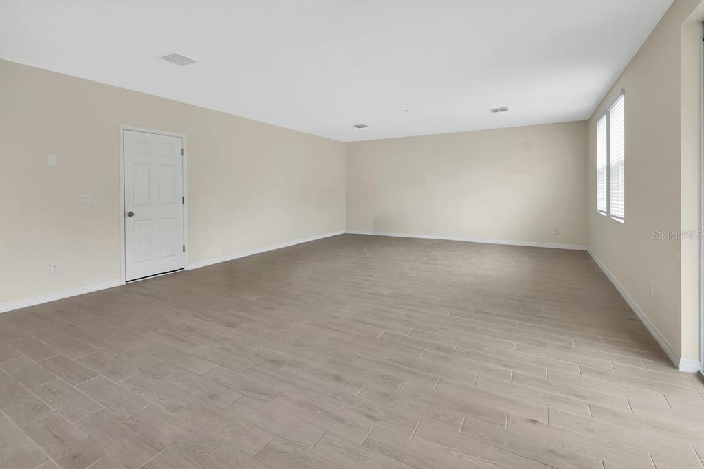 An empty room features light-colored walls, wood-look tile flooring, and a white door — 335 NW SARAH NICOLE WAY, NEW SMYRNA BEACH, FL