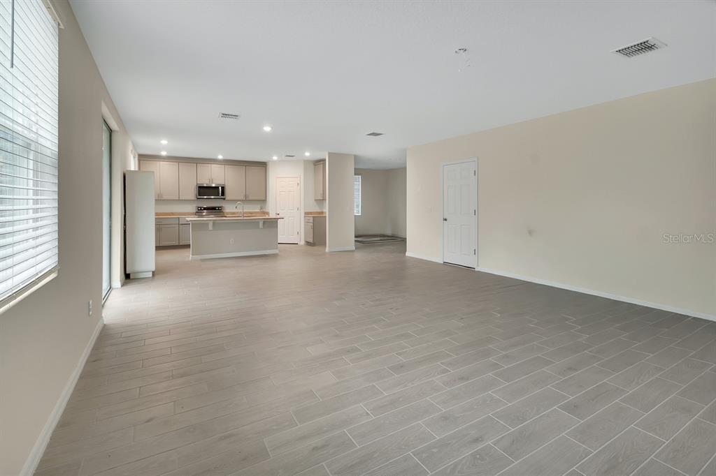 An open-concept living area features light gray wood-look tile flooring and a modern kitchen — 335 NW SARAH NICOLE WAY, NEW SMYRNA BEACH, FL