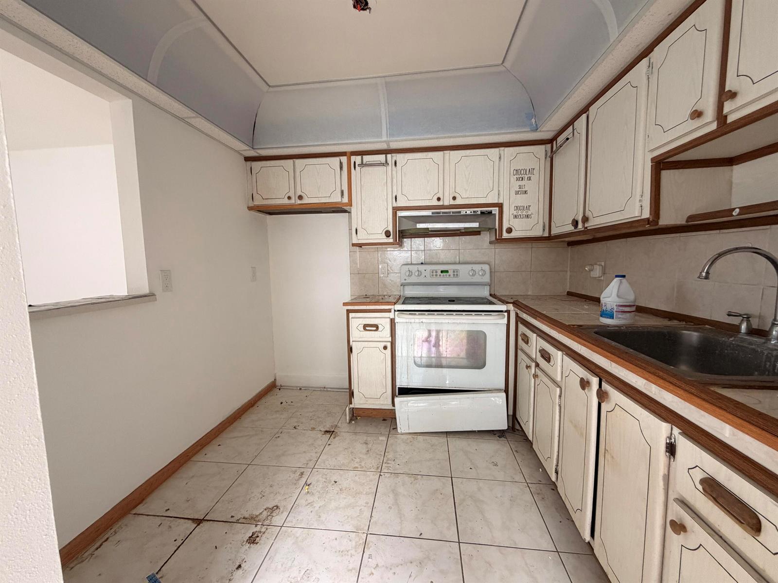A dated kitchen features white cabinets with wood trim, tile flooring, and a white stove — 355 Brittany H, Delray Beach FL 33446, DELRAY BEACH, FL