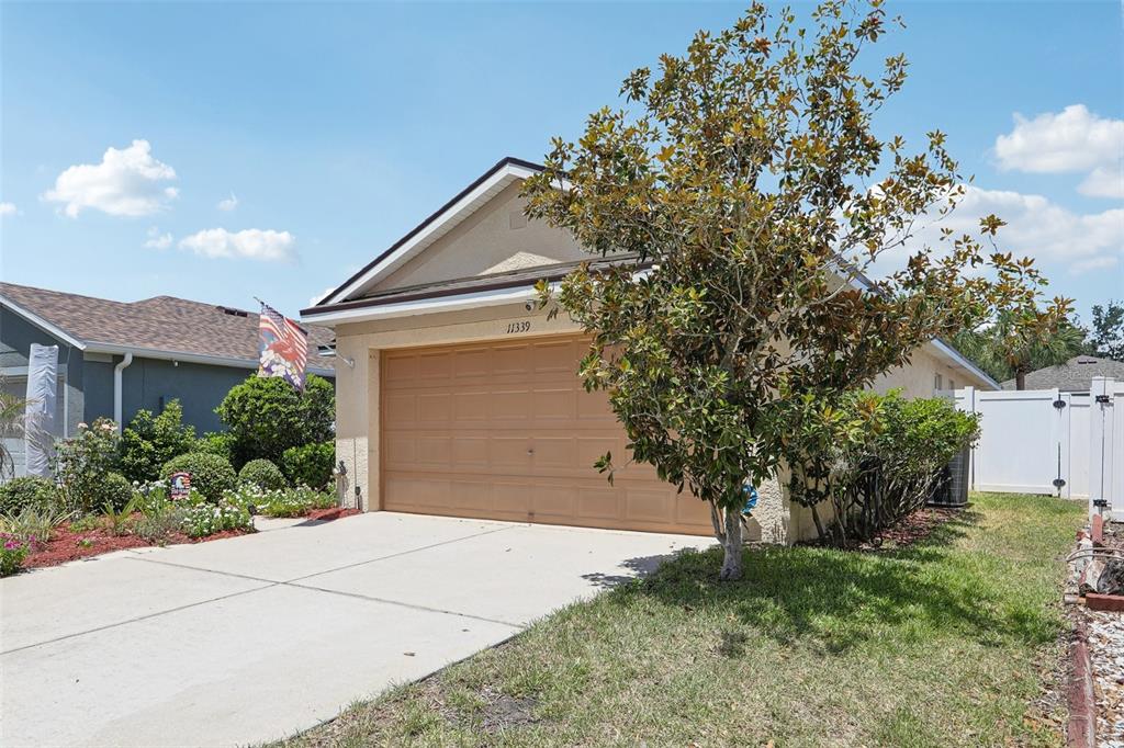 A tan house with a two-car garage and a large tree in the front yard — 11339 PALM ISLAND AVENUE, RIVERVIEW, FL