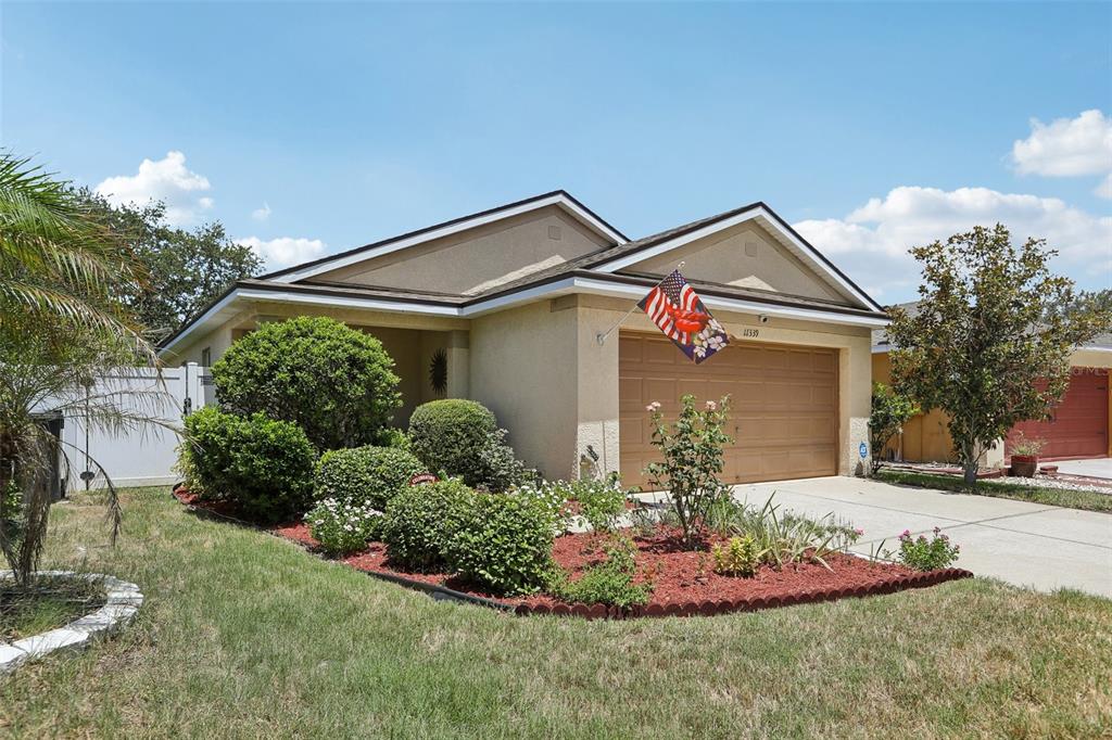 A single-story house with a tan stucco exterior, a two-car garage, and a landscaped front yard — 11339 PALM ISLAND AVENUE, RIVERVIEW, FL