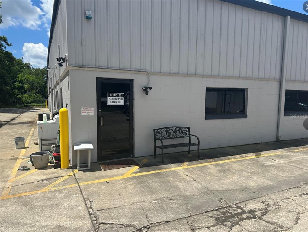 The exterior of a commercial building features a glass door, a metal bench, and bollards — 2920 W AIRPORT BOULEVARD UNIT 150, SANFORD, FL