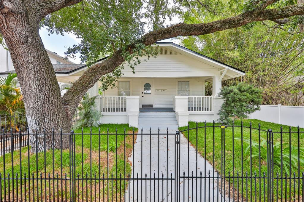 A white bungalow with a front porch and a large tree behind a metal fence — 902 W COLUMBUS DRIVE, TAMPA, FL