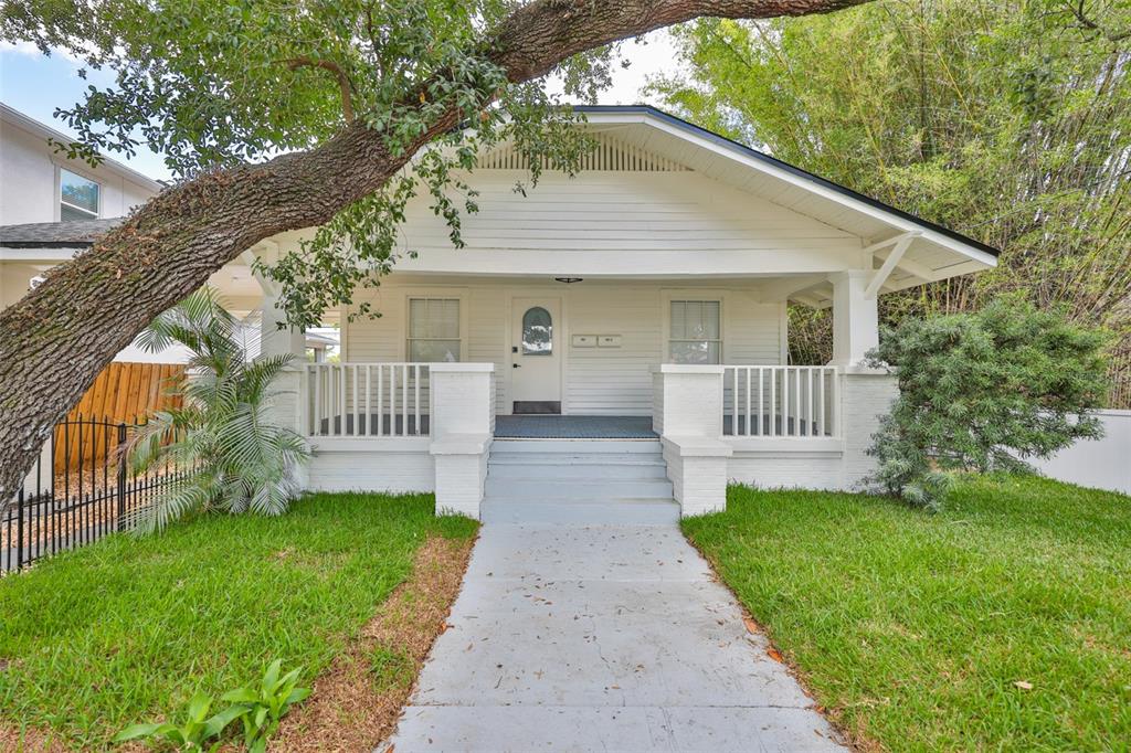 A white bungalow with a front porch and a large tree behind a black fence — 902 W COLUMBUS DRIVE, TAMPA, FL