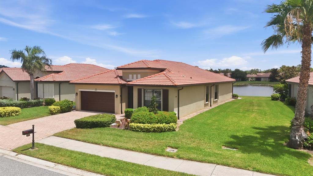 A single-story house with a tile roof, two-car garage, and a lawn beside a pond — 20252 PEZZANA DRIVE, VENICE, FL