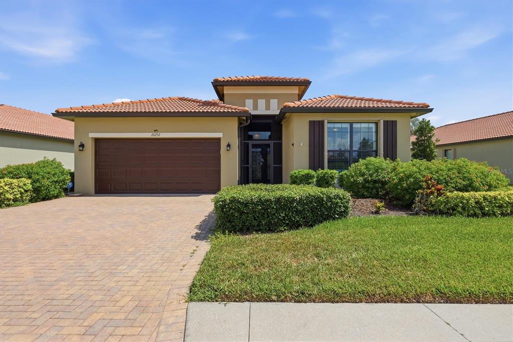 A single-story house with a tile roof, tan stucco exterior, and a paved driveway — 20252 PEZZANA DRIVE, VENICE, FL