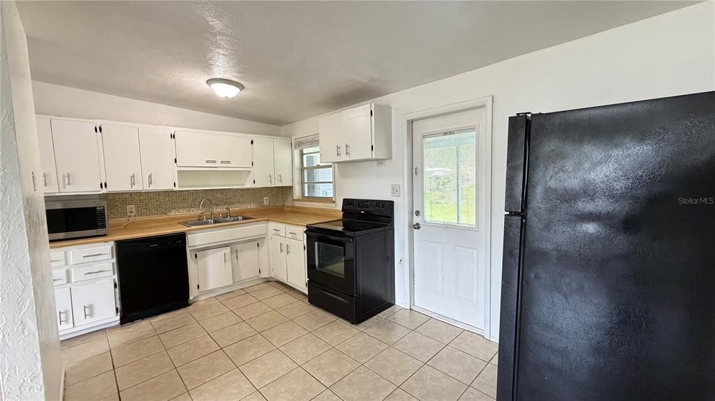A kitchen features white cabinets, black appliances, tan countertops, and light-colored tile flooring — 8574 94TH AVENUE, SEMINOLE, FL