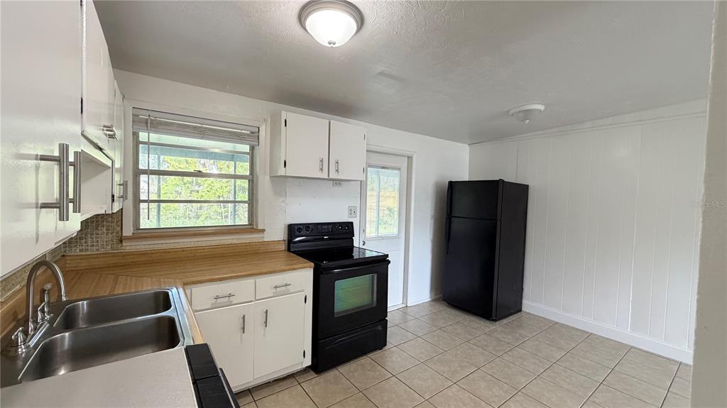 A kitchen with white cabinets, a black stove, a black refrigerator, and tile flooring — 8574 94TH AVENUE, SEMINOLE, FL