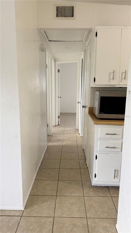 A hallway with tiled floors leads to a doorway, with white cabinets and a microwave nearby — 8574 94TH AVENUE, SEMINOLE, FL