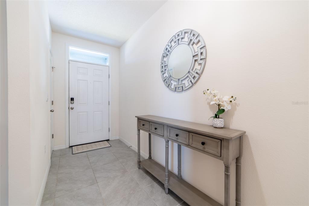 A foyer features gray tile flooring, a console table, and a circular decorative wall mirror — 2684 MAGNOLIA AVENUE, DAVENPORT, FL