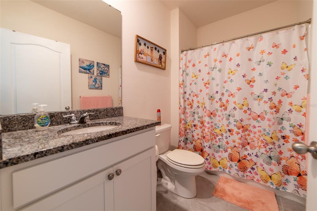 A bathroom features a granite-topped vanity, a white toilet, and a butterfly-patterned shower curtain — 2684 MAGNOLIA AVENUE, DAVENPORT, FL