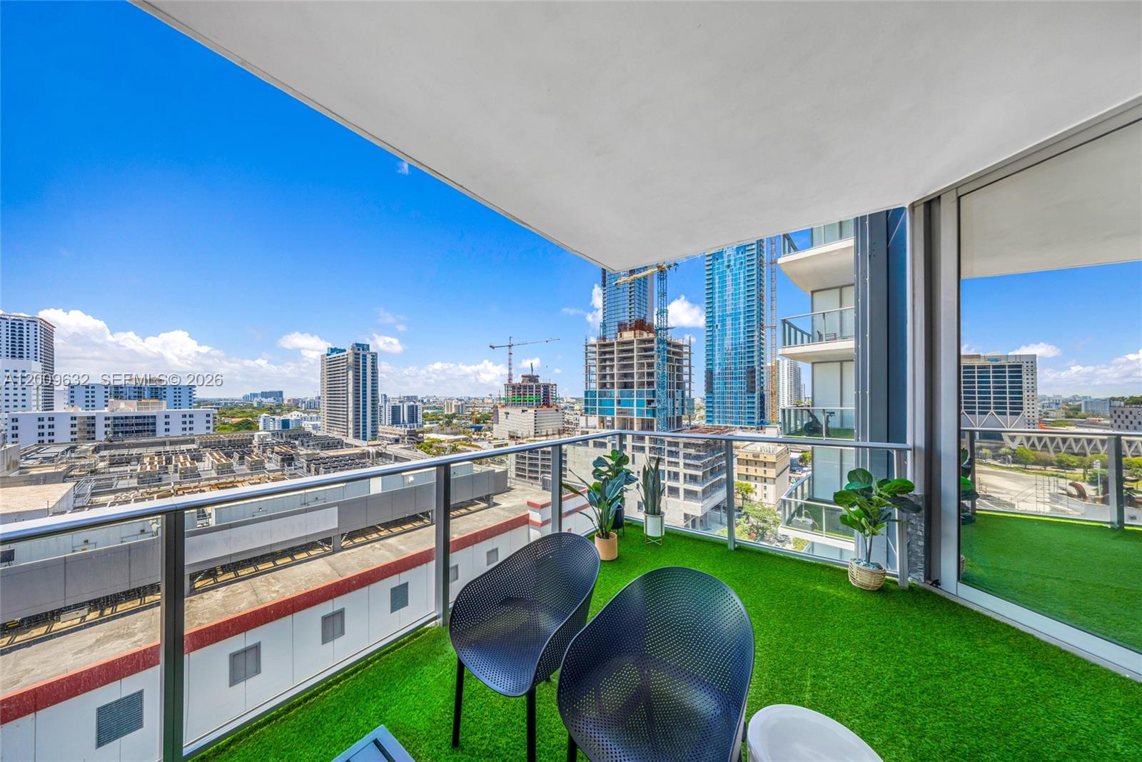 A balcony with artificial grass, two chairs, and potted plants overlooks a city skyline — 851 NE 1st Ave # 1408, Miami FL 33132, MIAMI, FL