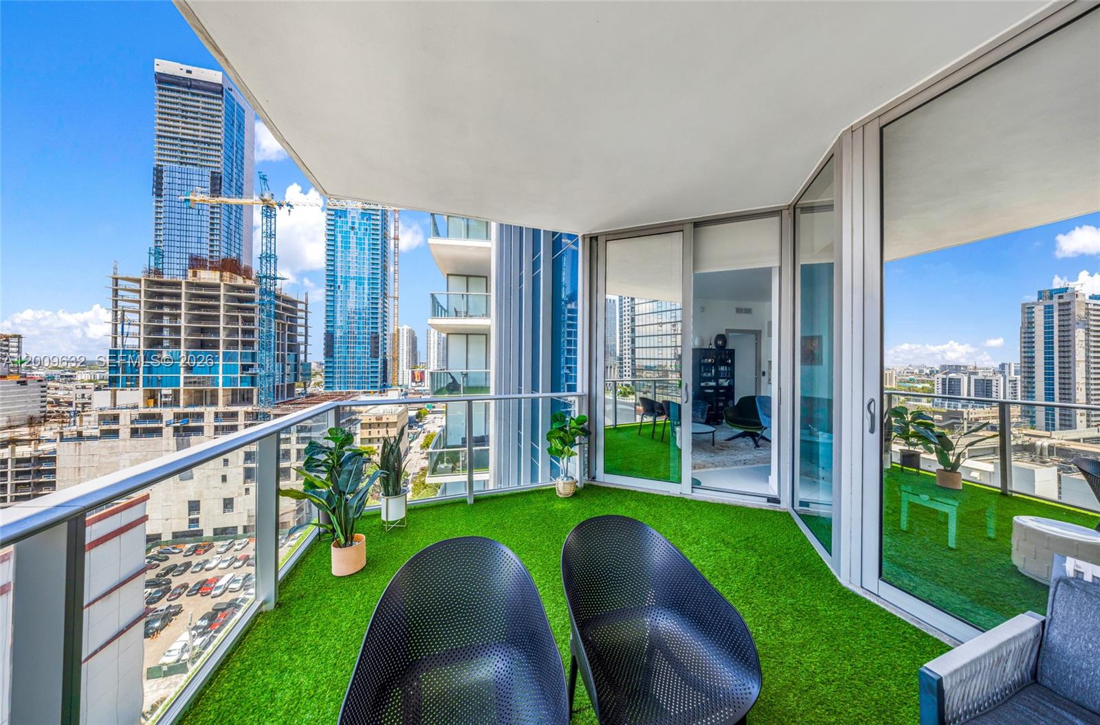 A balcony with artificial grass, two black chairs, and views of surrounding city skyscrapers — 851 NE 1st Ave # 1408, Miami FL 33132, MIAMI, FL