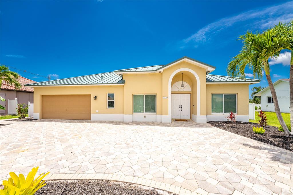 A single-story house with a yellow stucco exterior, metal roof, and a paved driveway — 3310 SW 26TH AVENUE, CAPE CORAL, FL