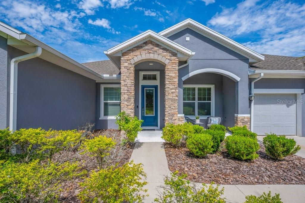 The exterior of a gray house features a stone-accented entryway and a blue front door — 1210 LOREA LANE, BRANDON, FL