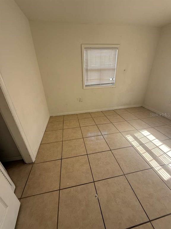 An empty room features beige tiled flooring, off-white walls, and a single window with blinds — 4638 AMERICA, ORLANDO, FL