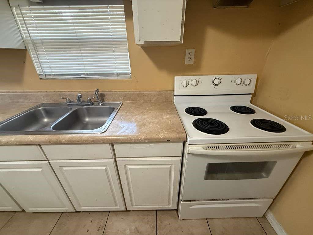 A kitchen features a stainless steel double sink, white cabinets, and a white electric stove — 4638 AMERICA, ORLANDO, FL