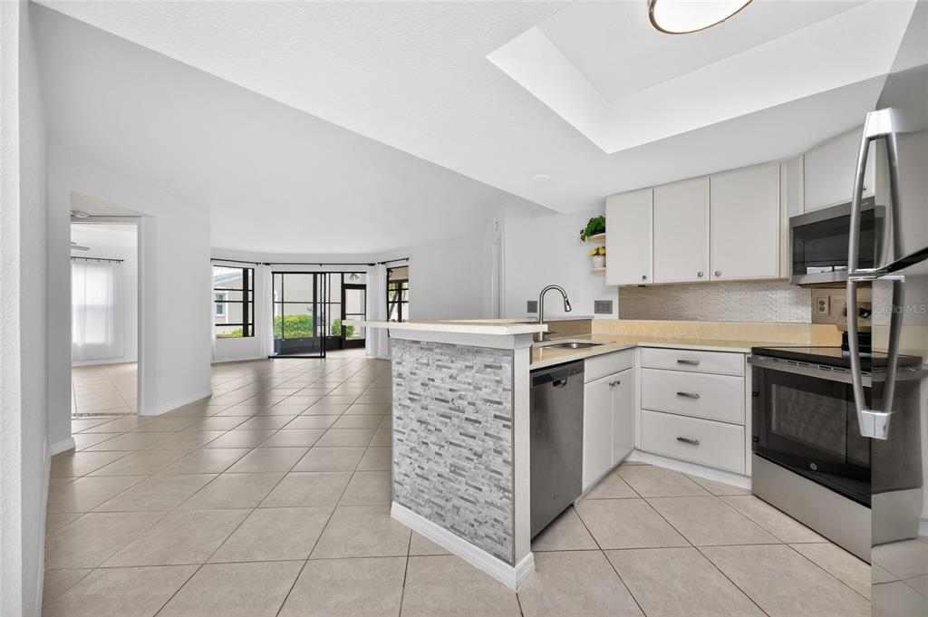 A kitchen with white cabinets and a stone-tiled breakfast bar opens to a living area — 2601 W MARION AVENUE UNIT 42A, PUNTA GORDA, FL