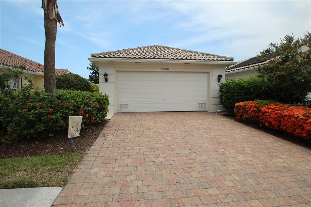 A paved driveway leads to a two-car garage with a tiled roof and landscaping — 5506 MODENA PLACE, SARASOTA, FL