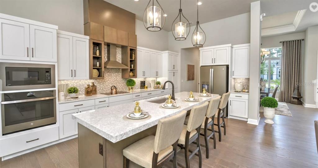 A modern kitchen features white cabinetry, a large marble-topped island, and stainless steel appliances — 17 KENSINGTON STREET, ORMOND BEACH, FL