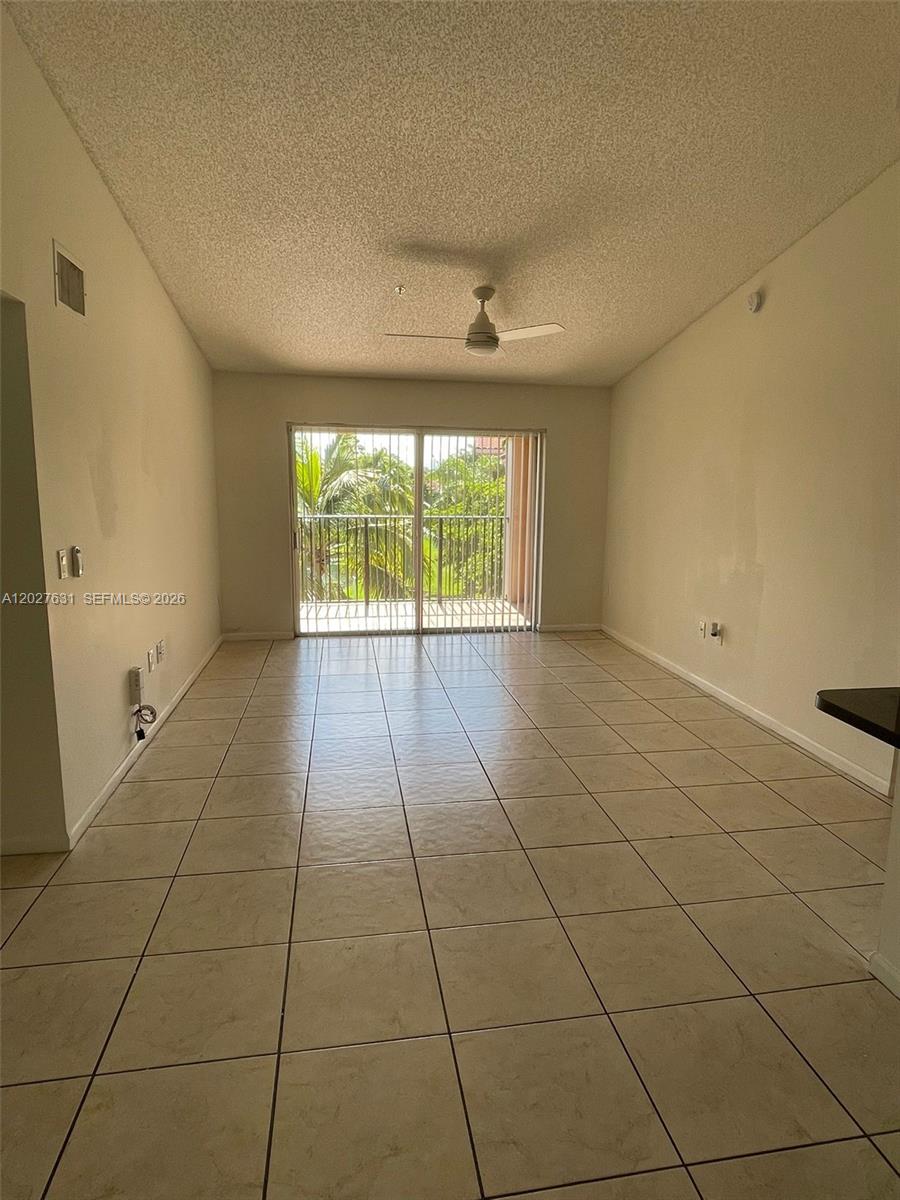 An empty living room features beige tile flooring, a ceiling fan, and a sliding glass door — 2081 Renaissance Blvd # 306, Miramar FL 33025, MIRAMAR, FL