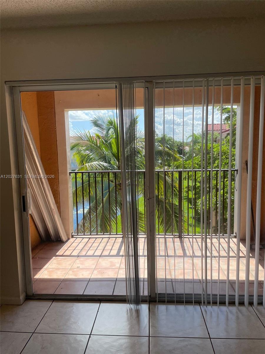 A sliding glass door opens onto a tiled balcony overlooking a palm tree and water — 2081 Renaissance Blvd # 306, Miramar FL 33025, MIRAMAR, FL