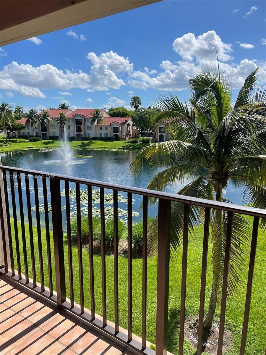 A balcony overlooks a lake with a fountain and apartment buildings under a blue sky — 2081 Renaissance Blvd # 306, Miramar FL 33025, MIRAMAR, FL