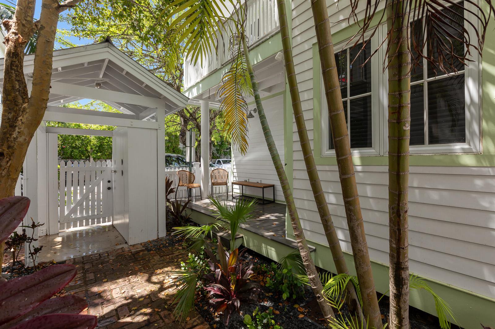 A white house with a porch, palm trees, and a brick walkway leading to a gate — 1011 Simonton Street # 1, Key West FL 33040, KEY WEST, FL