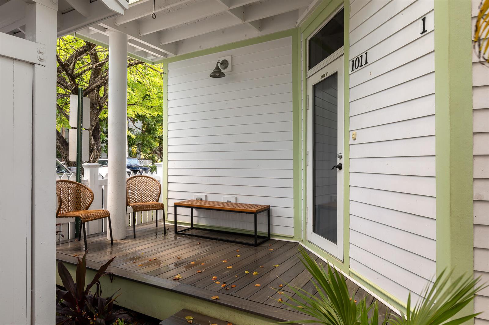 A covered wooden porch features two wicker chairs, a bench, and a glass-paneled front door — 1011 Simonton Street # 1, Key West FL 33040, KEY WEST, FL