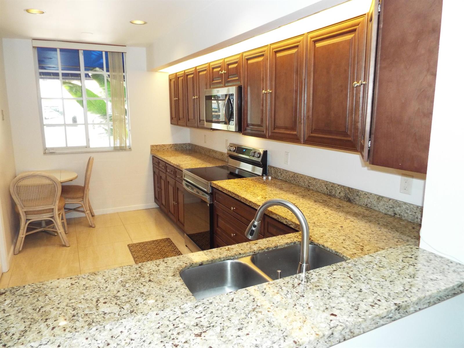 A kitchen features dark wood cabinets, granite countertops, stainless steel appliances, and a dining area — 4128 W Palm Aire Drive # 281b, Pompano Beach FL 33069, POMPANO BEACH, FL