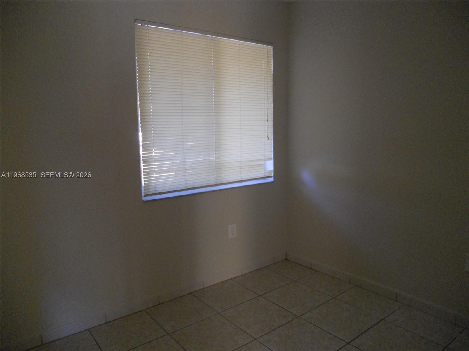 An empty room features light-colored tile flooring, plain walls, and a window with closed blinds — 22 SW 14th Ter, Homestead FL 33030, HOMESTEAD, FL