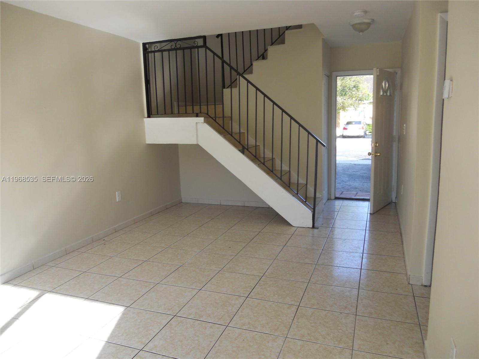 An interior view shows a tiled living area with a staircase and an open door — 22 SW 14th Ter, Homestead FL 33030, HOMESTEAD, FL
