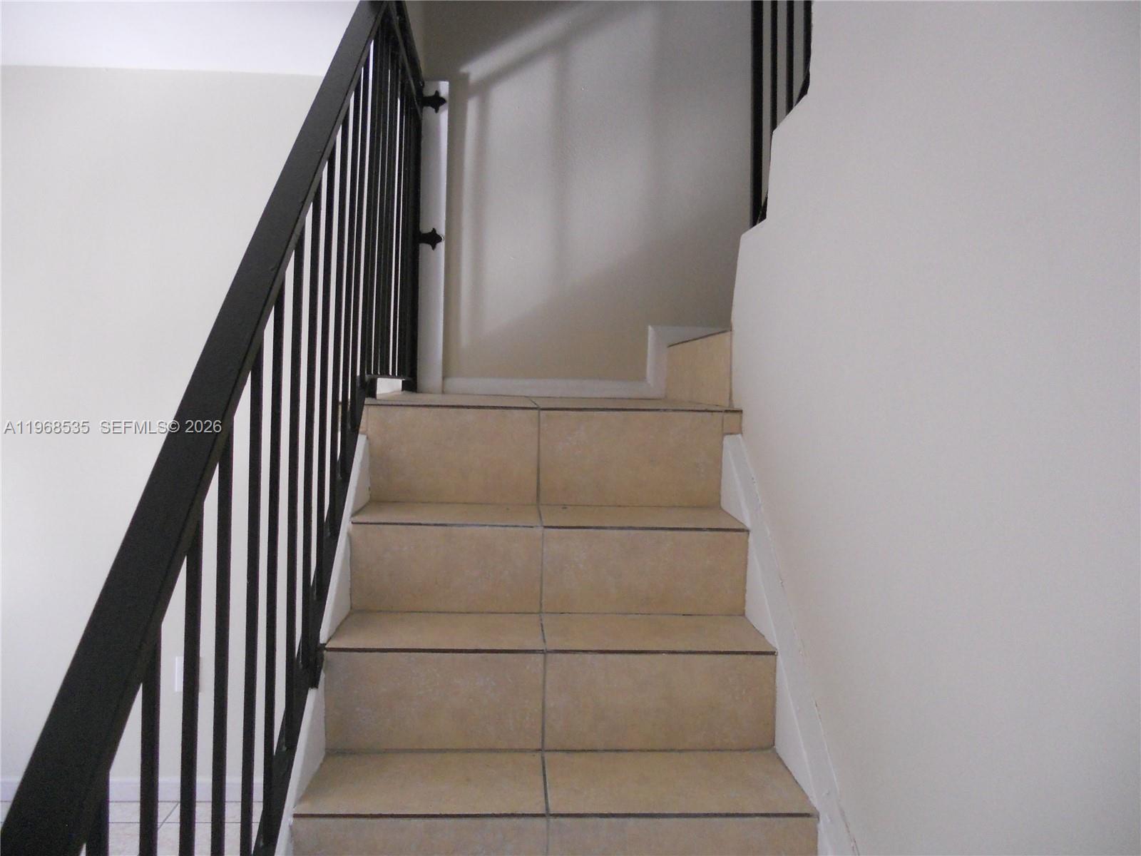 A staircase with beige tiled steps and a black metal railing leads to a landing — 22 SW 14th Ter, Homestead FL 33030, HOMESTEAD, FL