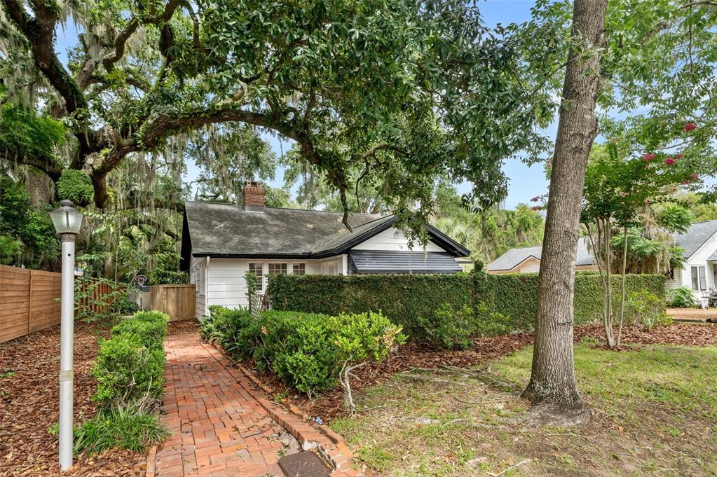 A brick walkway leads to a white cottage with a dark roof and a hedge — 16 NW 20TH TERRACE, GAINESVILLE, FL