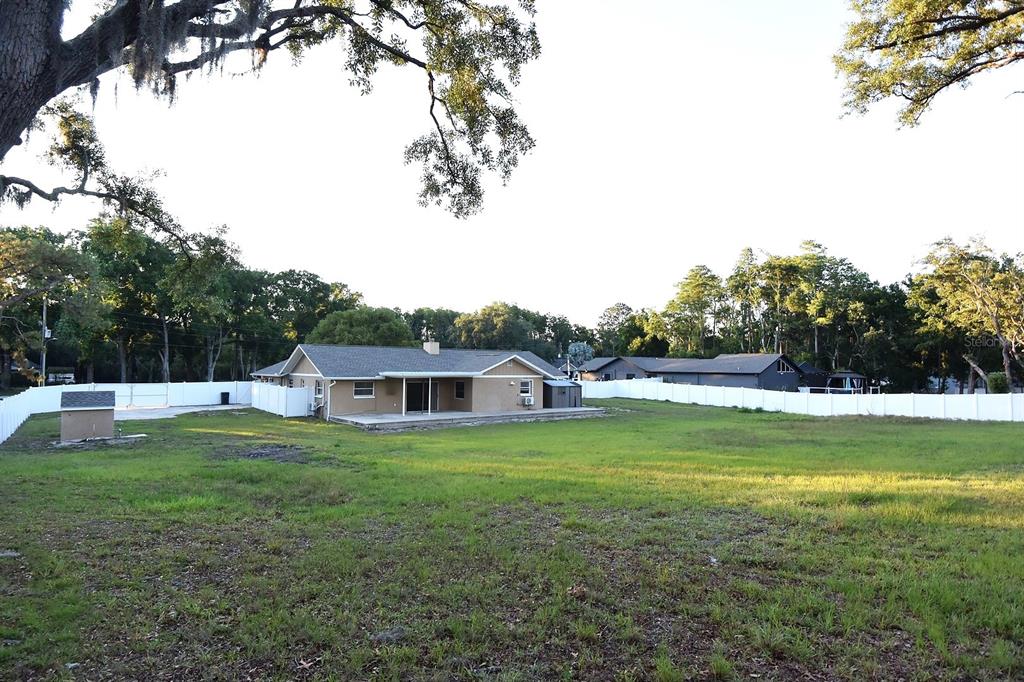 A tan house with a large backyard and white vinyl fencing under a clear sky — 6848 COPPERFIELD DRIVE, NEW PORT RICHEY, FL