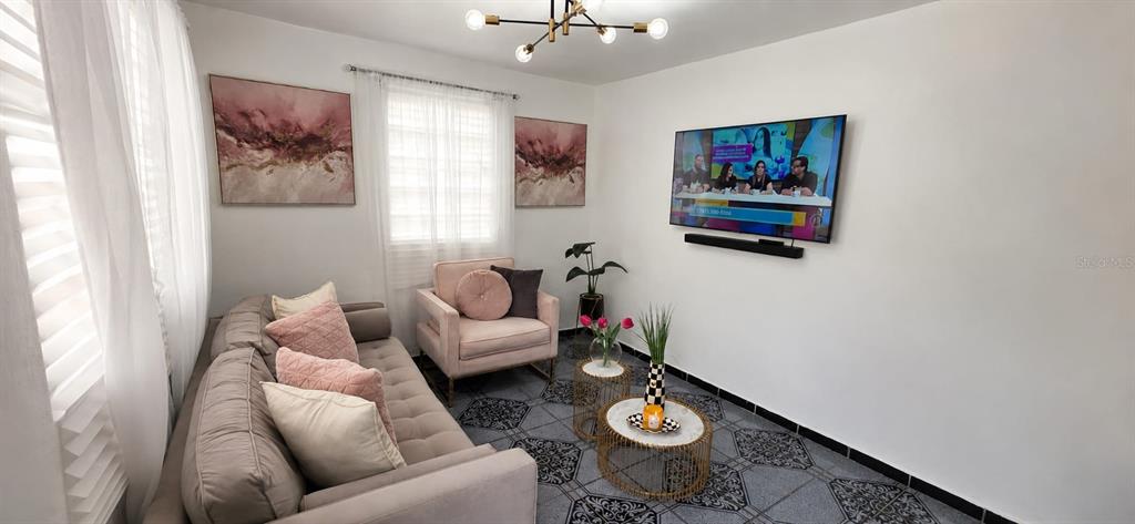A living room features a gray sofa, a pink armchair, two round tables, and a television — calle 10 Int. PARCELAS VANSCOY, BAYAMON, PR