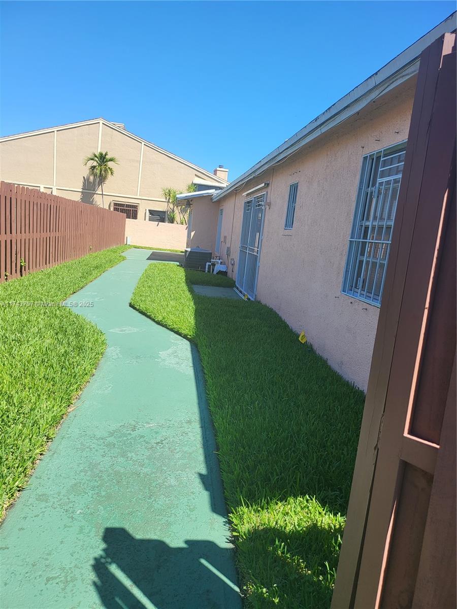 A side yard features a green painted walkway, a lawn, and a peach-colored house exterior — 6771 NW 199th Ter, Hialeah FL 33015, HIALEAH, FL
