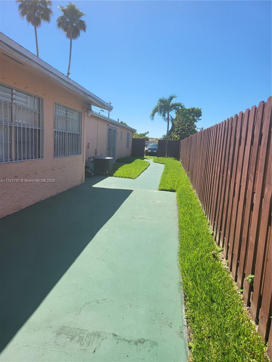 A side yard features a green concrete path, a wooden fence, and a pink house — 6771 NW 199th Ter, Hialeah FL 33015, HIALEAH, FL